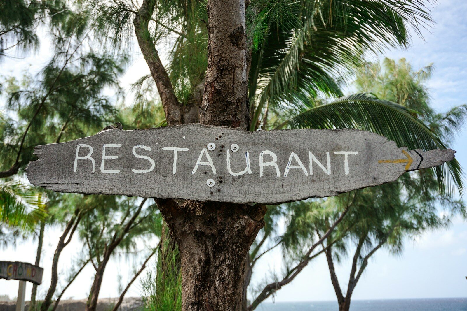 a wooden sign pointing to a restaurant next to the ocean